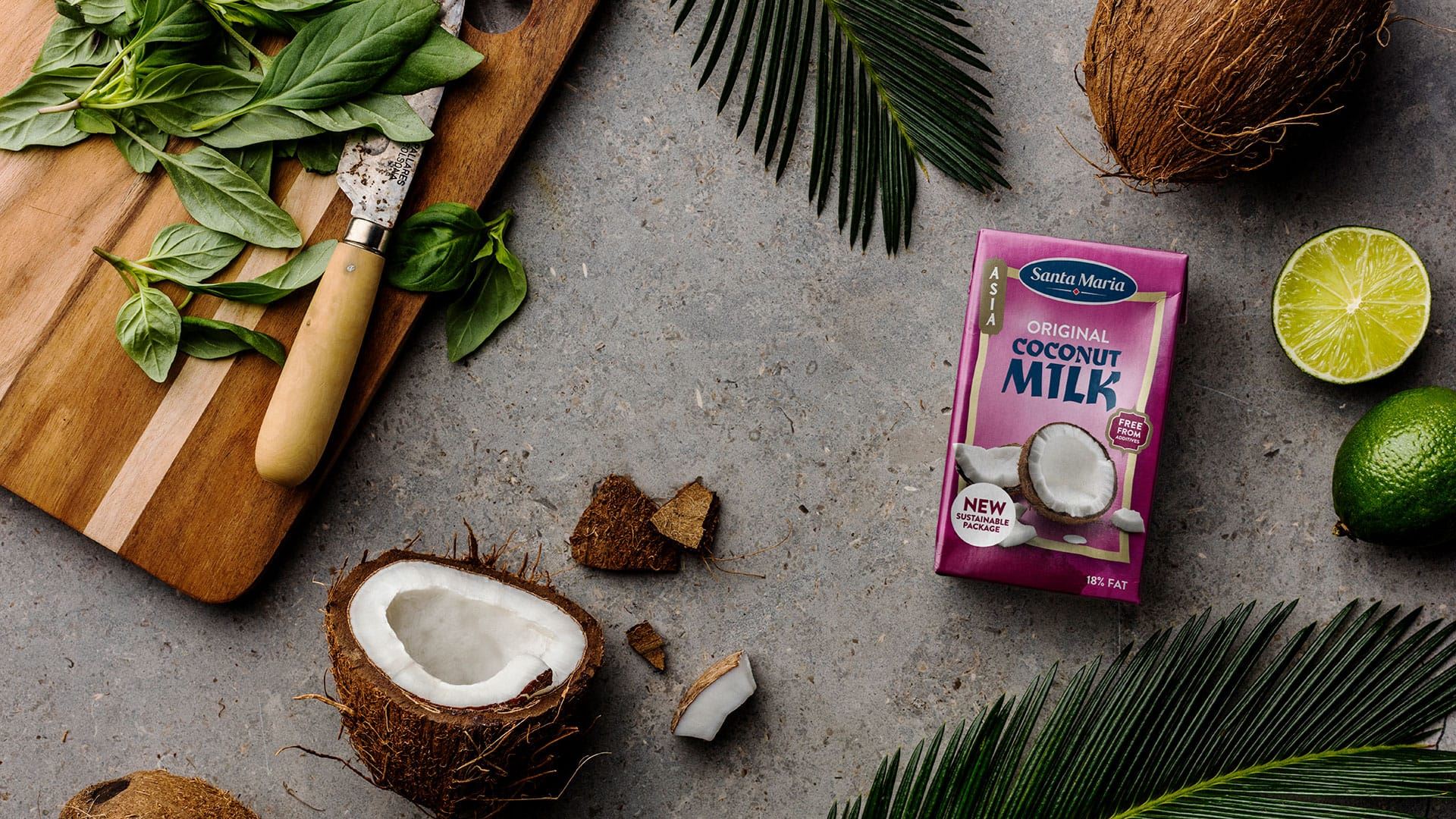 En förpackning med kokosmjölk ligger tillsammans med kokosnötter och en skärbräda