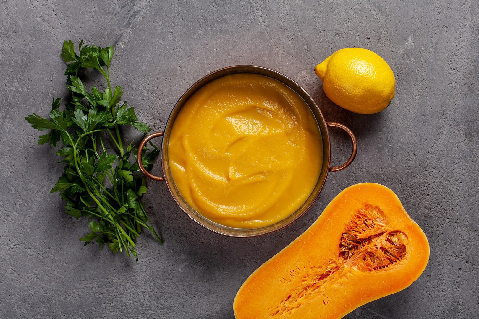 Pumpkin puree in a saucepan surrounded by lemon, butternut squash and leaf parsley