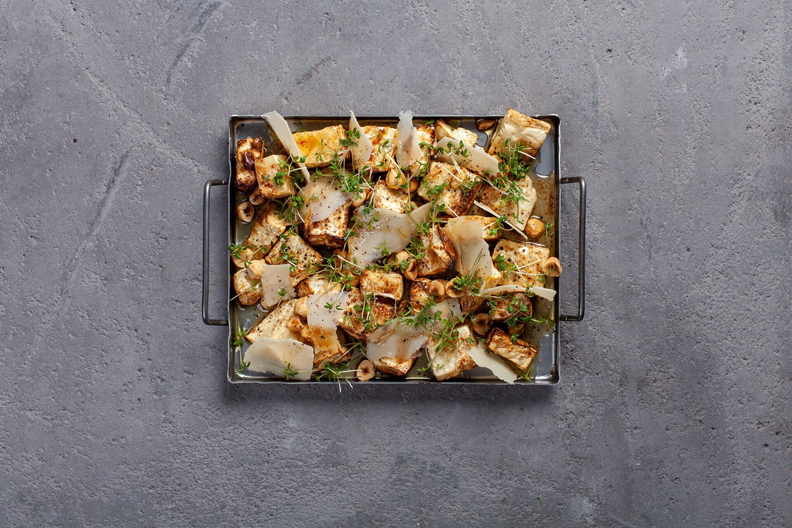 Small oven tray with roasted celeriac topped with parmesan and hazel nuts
