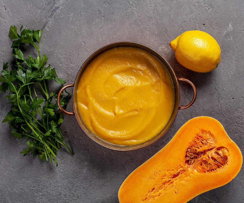Pumpkin puree in a saucepan surrounded by lemon, butternut squash and leaf parsley