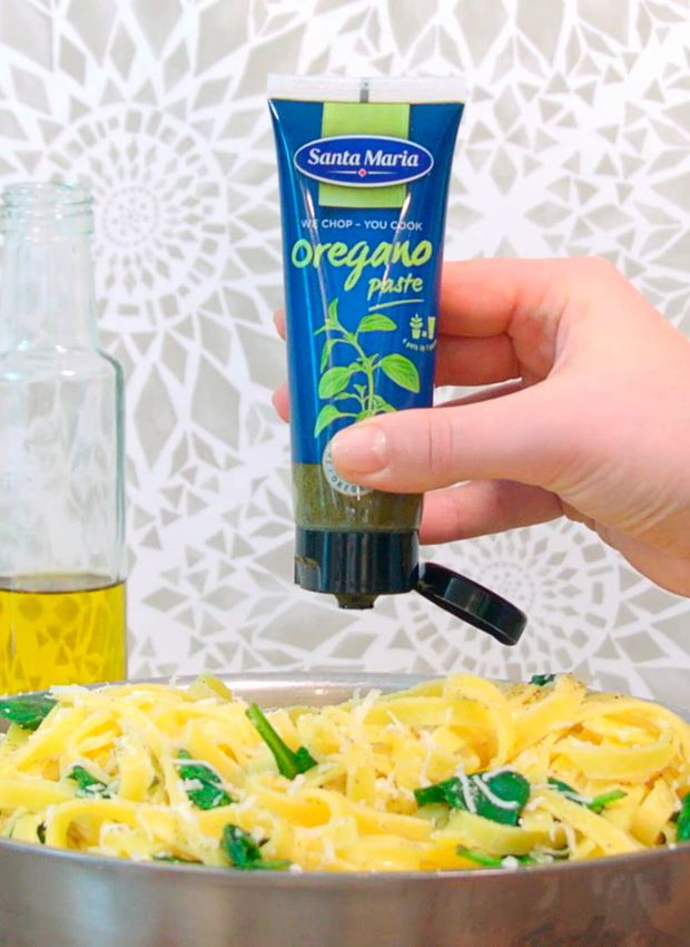 Hand som håller en tub med Oregano Paste över en panna med pasta.