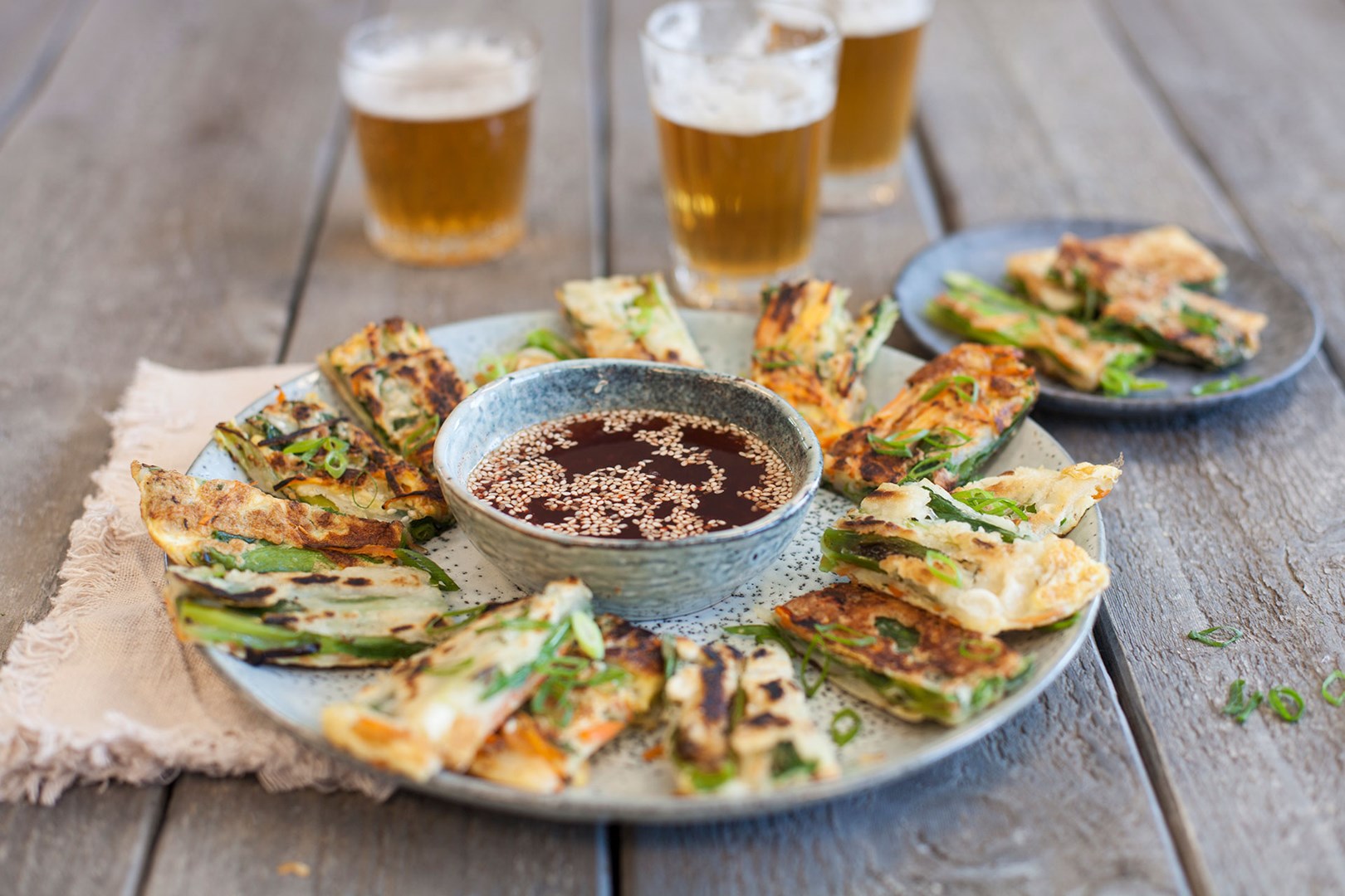 Pajeon - koreanska pannkakor upplagda på ett fat med en skål med dippsås i mitten.