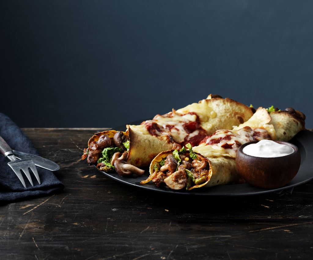 2 vega enchilada's gevuld met champignons en groenten geserveerd op een bord met een bakje zure room