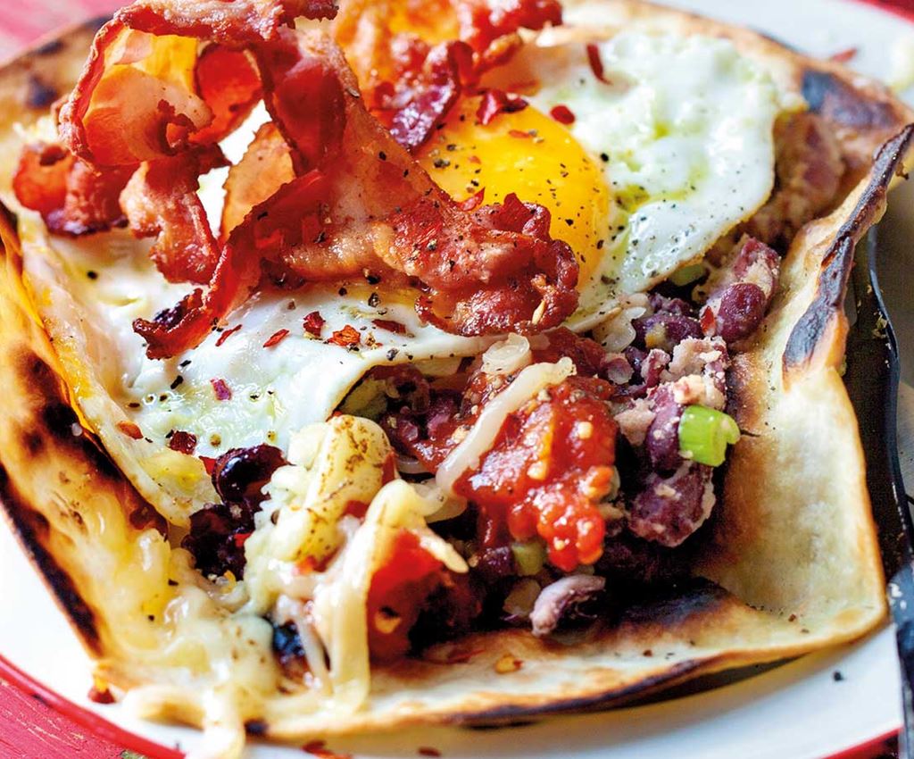 Open breakfast tortilla with fried eggs, grilled tomatoes, salsa and baked beans