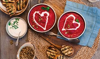 Two bowls of beetroot soup garnished with a heart of garlic yoghurt. Served with garlic bread